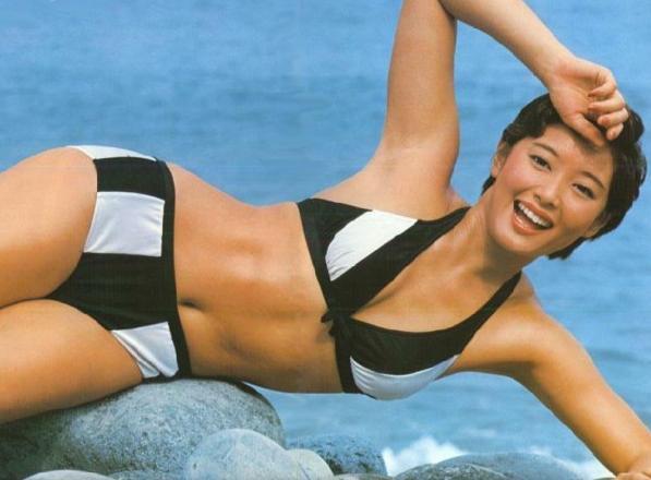 夏目雅子が黒と白のストライプのビキニで右手を上げ脇を見せる